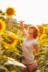 red-haired girl is standing next to a tall sunflower, a woman measures the height of a sunflower, her hand is lifted up