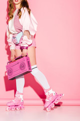 cropped view of stylish girl holding retro boombox while standing in roller-skates on pink