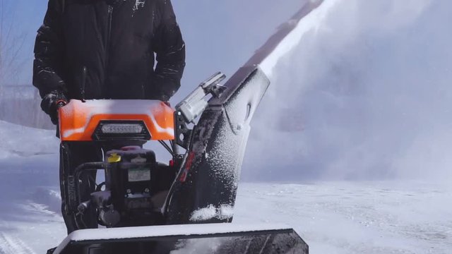 A man cleans the snow with a snowblower during a snowfall. Slow motion.