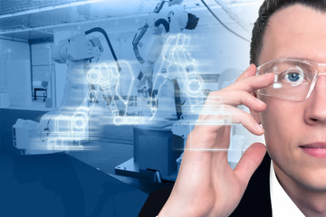 The engineer uses a glasses with augmented reality to control robots in a smart factory. Digital...