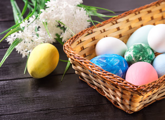 Fototapeta na wymiar Easter eggs in a basket and white flowers in a dark wooden background