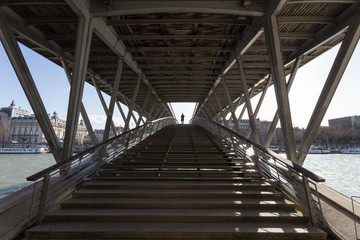 Perspective view on the Léopold-sédar-senghor bridge and its structure in Paris, with a man walking on the bridge.