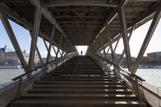 Perspective view on the L&eacute;opold-s&eacute;dar-senghor bridge and its structure in Paris, with a man walking on the bridge.