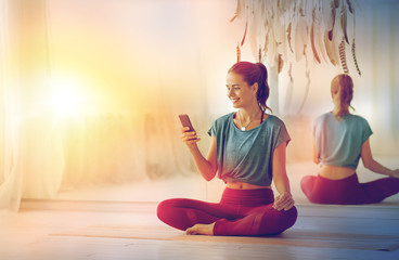 fitness, technology and healthy lifestyle concept - woman with smartphone at yoga studio with soft...
