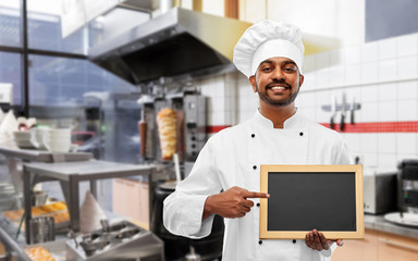 cooking, profession and people concept - happy male indian chef in toque with blank chalkboard for...