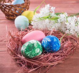 Easter eggs in a nest and white flowers on a wooden background