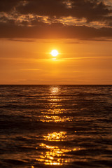 colorful sunset over calm sea beach with dark blue water and dramatic contrasty clouds