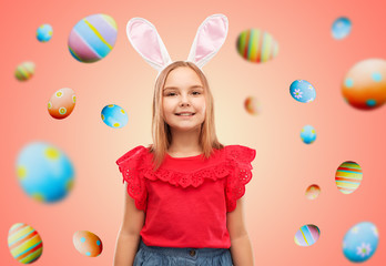 easter, holidays and childhood concept - happy girl wearing bunny ears headband over living coral background and colored eggs