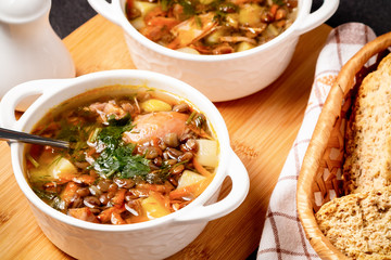 Two plates with lentil soup and chicken on a wooden board on black table