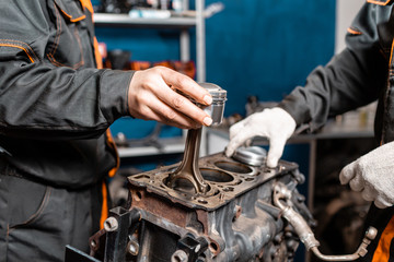 Two mechanic holding a new piston for the engine, overhaul.. Engine on a repair stand with piston and connecting rod of automotive technology. Interior of a car repair shop.