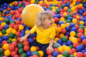 Fototapeta na wymiar Portrait of a blond boy in a yellow t-shirt. The child smiles and plays in the children's playroom. Ball pool.