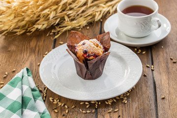 Blueberry muffin in brown paper with cup of tea on wooden table