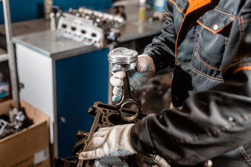 Close-up Car mechanic holding a new piston for the engine, overhaul.. Engine on a repair stand with piston and connecting rod of automotive technology. Interior of a car repair shop.