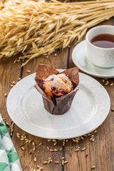 Blueberry muffin in brown paper with cup of tea on wooden table