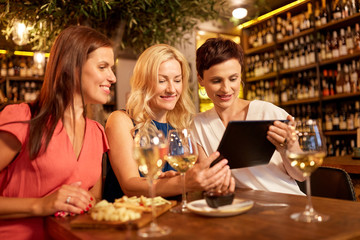 leisure, technology and lifestyle concept - happy women with tablet pc computer at wine bar or...
