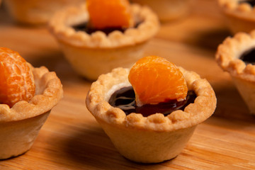 Sweet tartlets with chocolate and slices of tangerine on wooden dish for serving, close-up