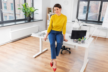business and people concept - happy businesswoman sitting on desk at office