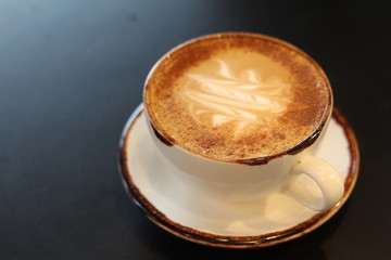 Latte art work in a cup on a plate on a black table