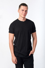 Obraz premium Handsome young smiling man wearing a black cotton short-sleeved T-shirt and black jeans posing in studio.