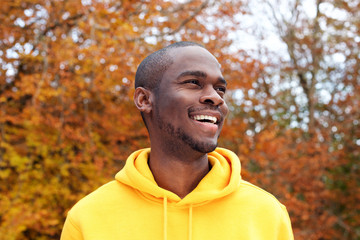 Close up handsome young african american man smiling against autumn leaves in background