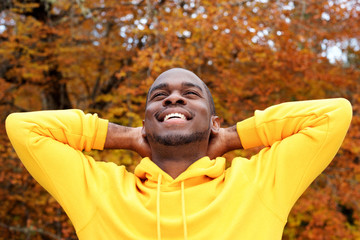  handsome young african american man against autumn leaves in background smiling with hands behind head