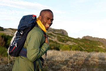 happy african american man hiking with backpack in the mountains