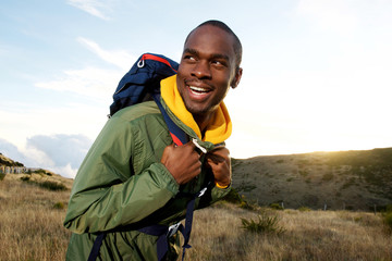 smiling african american man with backpack hiking in mountains