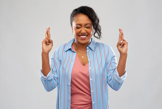 people, gesture and portrait concept - happy african american young woman holding fingers crossed over grey background