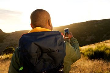 behind of african american man hiking with mobile phone taking selfie in mountains