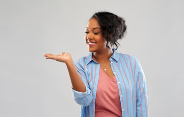 people and advertisement concept - happy african american young woman holding something imaginary on empty hand over pink background - Powered by Adobe