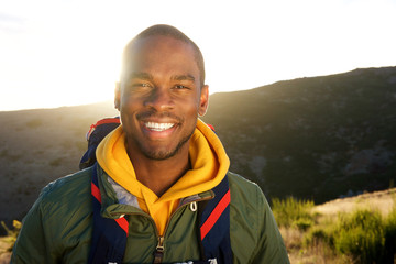 Close up handsome young african american man with back pack posing in nature with sunset in...