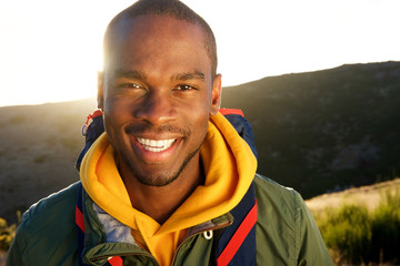 Close up smiling young black man hiking in mountains with backpack