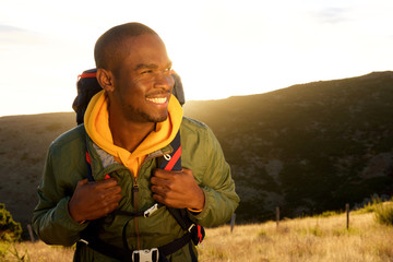 Close up handsome young african american man with backpack smiling with sunset in background