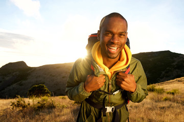 happy african american man hiking in mountains with backpack and sunset in background - Powered by Adobe