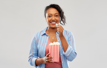 fast food and people concept - happy african american young woman eating popcorn from striped...