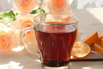 Tea in a cup and lemon on a sunny table. A bouquet of cream roses in the background creates a good mood of a spring morning and a good day.