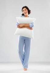 people and bedtime concept - happy young woman in blue pajama hugging pillow over grey background