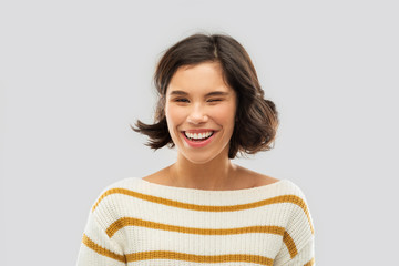 Fototapeta premium expression and people concept - happy smiling young woman in striped pullover winking over grey background
