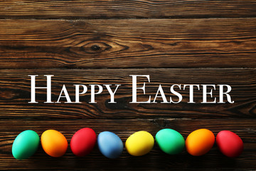 Happy Easter text with different colorful boiled paintd eggs. Greeting card concept with traditional holiday attributes. Wood textured table top background, close up, top view, copy space, flat lay.