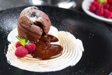 Chocolate pudding lava cake with vanilla cream, raspberry and mint on a black plate. Sweet muffins for dessert