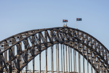 Sydney, Australia - February 12, 2019: Closeup of Harbour bridge span during sunset. Black metal, Flags and light blue sky.