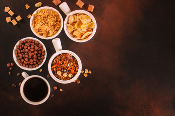 cornflakes, coffee, bread, butter, eggs, jam and other ingredients for breakfast on a dark background. Top view with copy space