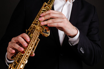Naklejka premium Saxophonist in black classic suit playing soprano saxophone in jazz orchestra close-up