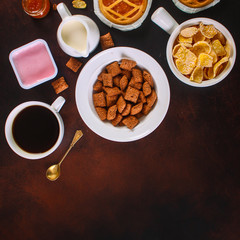 cornflakes, coffee, bread, butter, eggs, jam and other ingredients for breakfast on a dark background. Top view with copy space