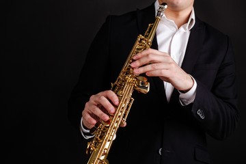 Fototapeta na wymiar Saxophonist in a black classic suit playing the soprano saxophone