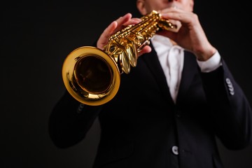 Saxophonist in a black classic suit playing the soprano saxophone close-up