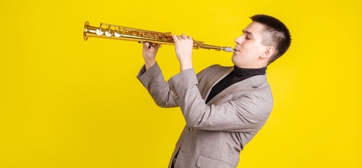 Saxophonist plays soprano saxophone on yellow background side view