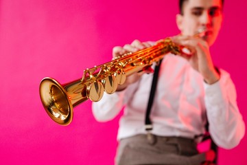 Male saxophonist to not focus on playing jazz on the soprano saxophone while standing on a pink...