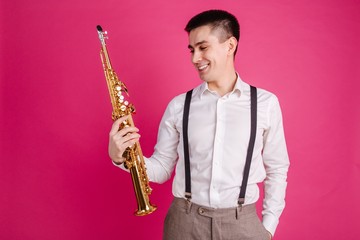 Naklejka premium Saxophonist holding a saxophone in his hand on a pink background