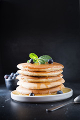 Sweet homemade stack of pancakes with fresh blueberry and mint in modern plate on black background.